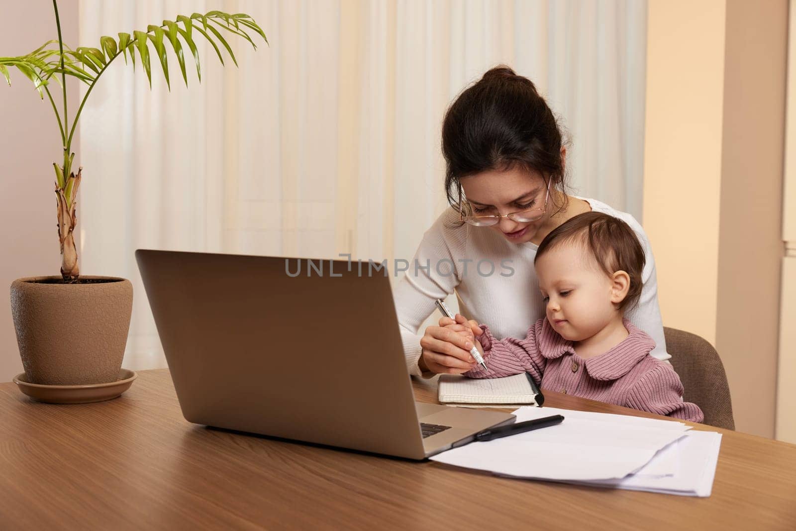 Cheerful pretty businesswoman working on laptop at home with her little child girl