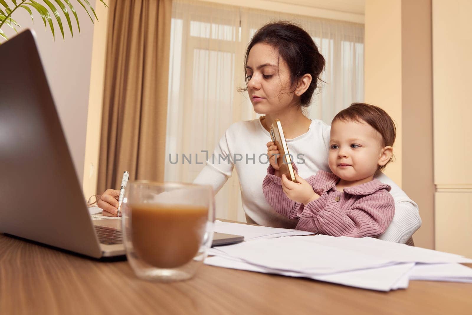Cheerful pretty businesswoman working on laptop at home with her little child girl