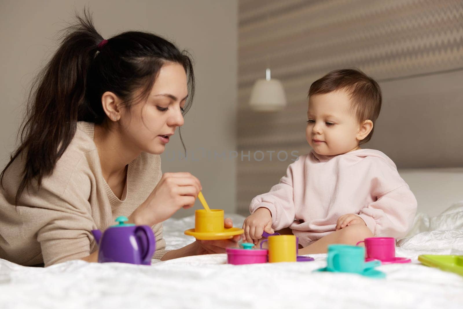 Attractive mother and little child daughter playing tea party and spending time together in bedroom, family having fun