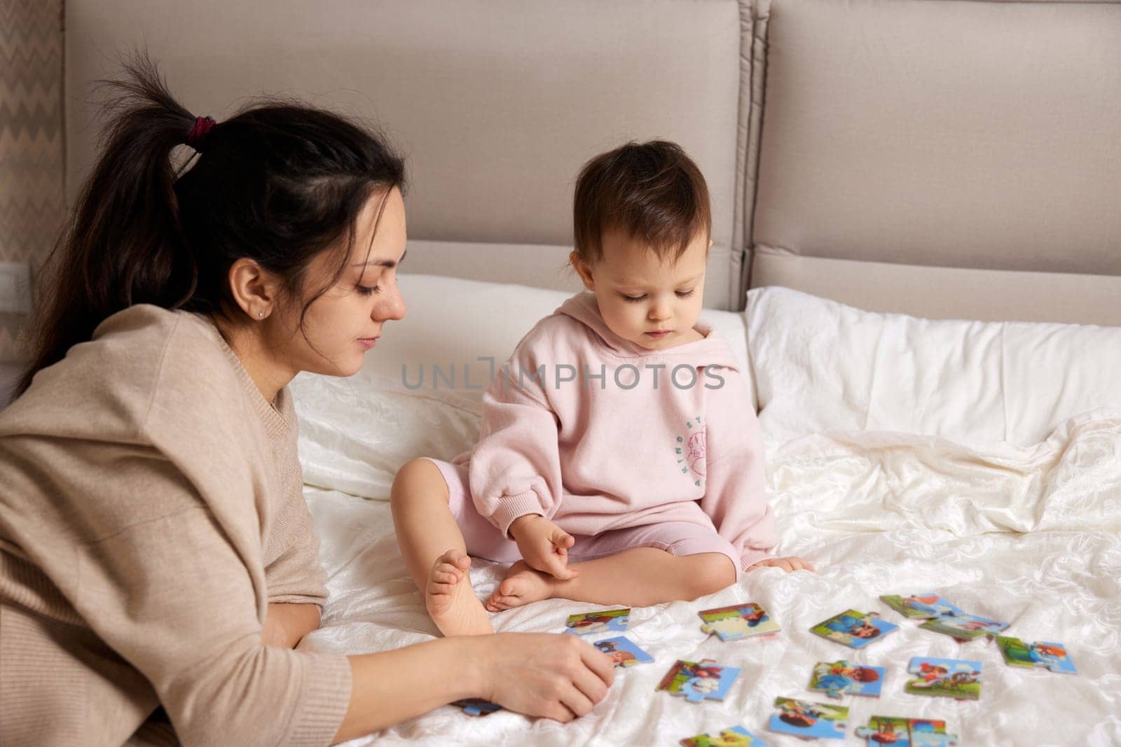 pretty mother playing puzzle together with her little child girl in bedroom