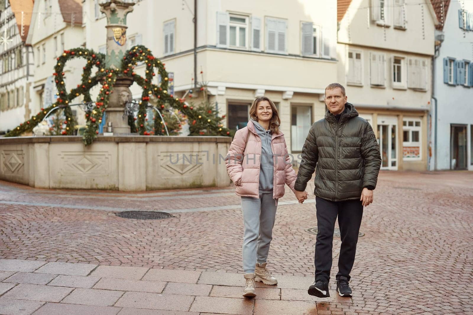 Loving couple of tourists walking around old town. Couple of lovers leisurely stroll in the cool autumn morning on the streets of a BIETIGHEIM-BISSINGEN (Germany). The guy holds his wife. Vacation, Winter, holiday. Romantic Stroll through Historic German Charm. Couple Walking in Europe's Old Town by Andrii_Ko