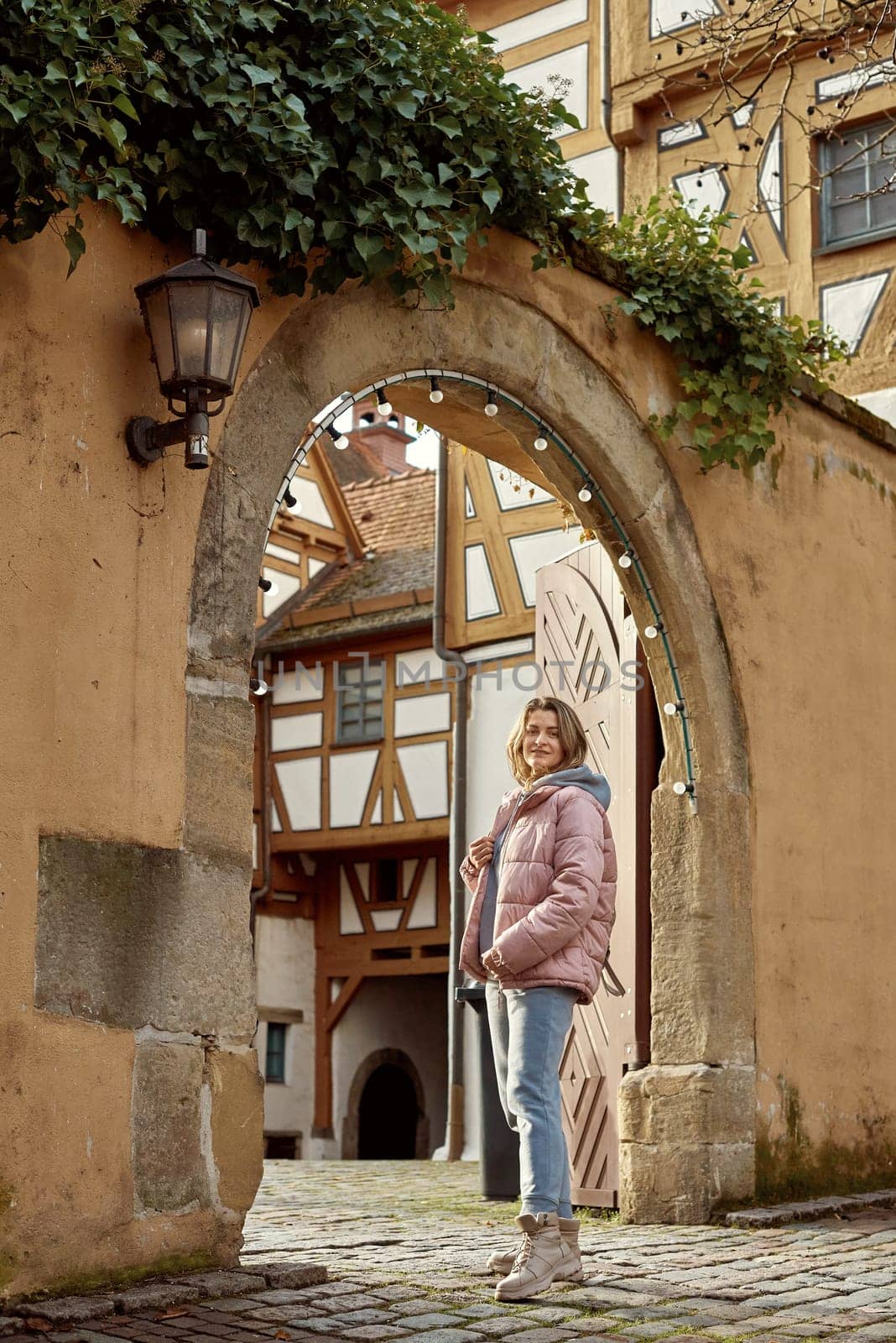 Winter Fun in Bitigheim-Bissingen: Beautiful Girl in Pink Jacket Amidst Half-Timbered Charm. a lovely girl in a pink winter jacket standing in the archway of the historic town of Bitigheim-Bissingen, Baden-Württemberg, Germany. by Andrii_Ko