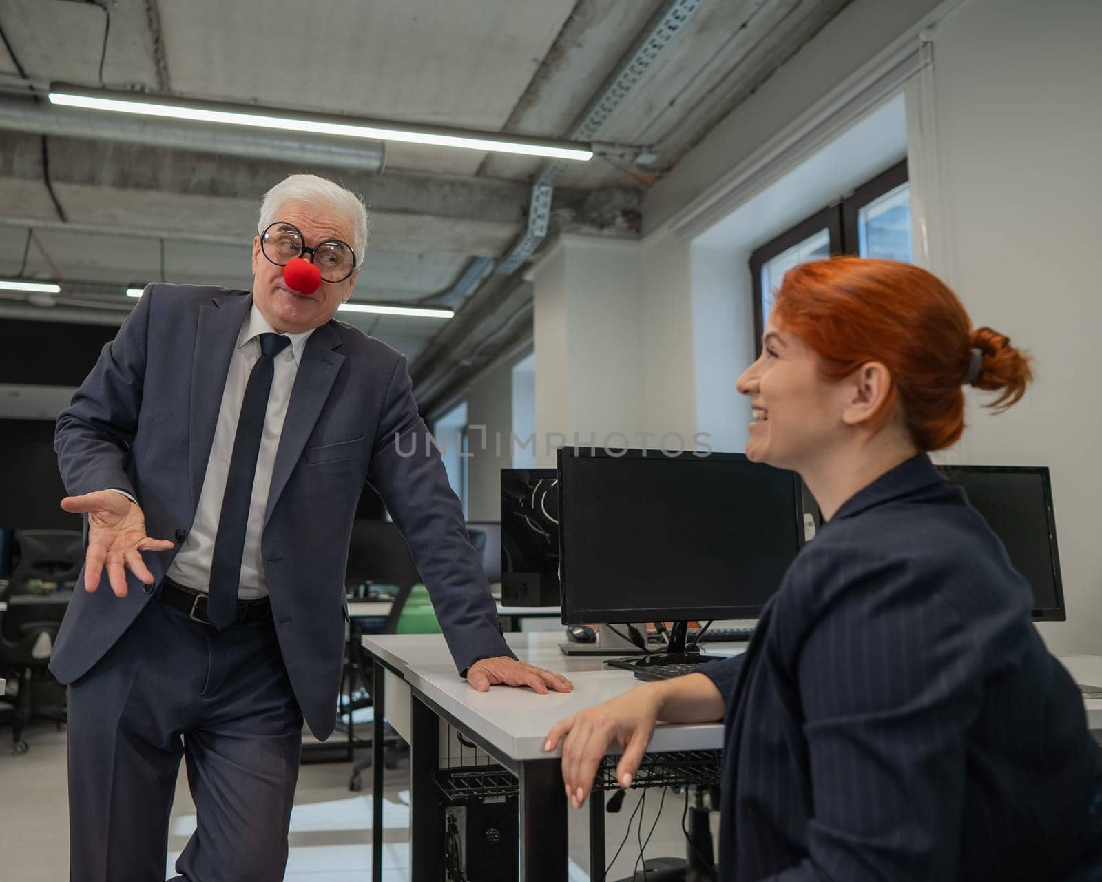 Caucasian woman communicates with an elderly man in a clown costume in the office. by mrwed54