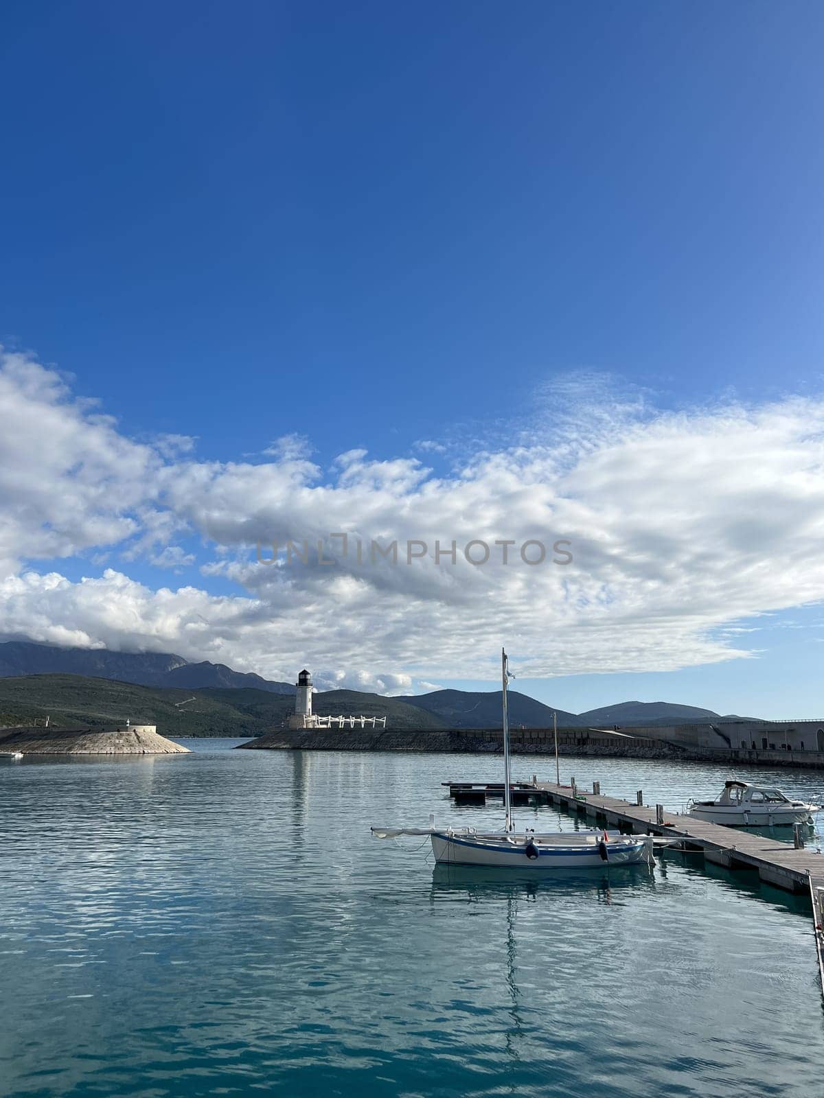 Boats moored at the pier against the backdrop of a lighthouse at the foot of the mountains by Nadtochiy