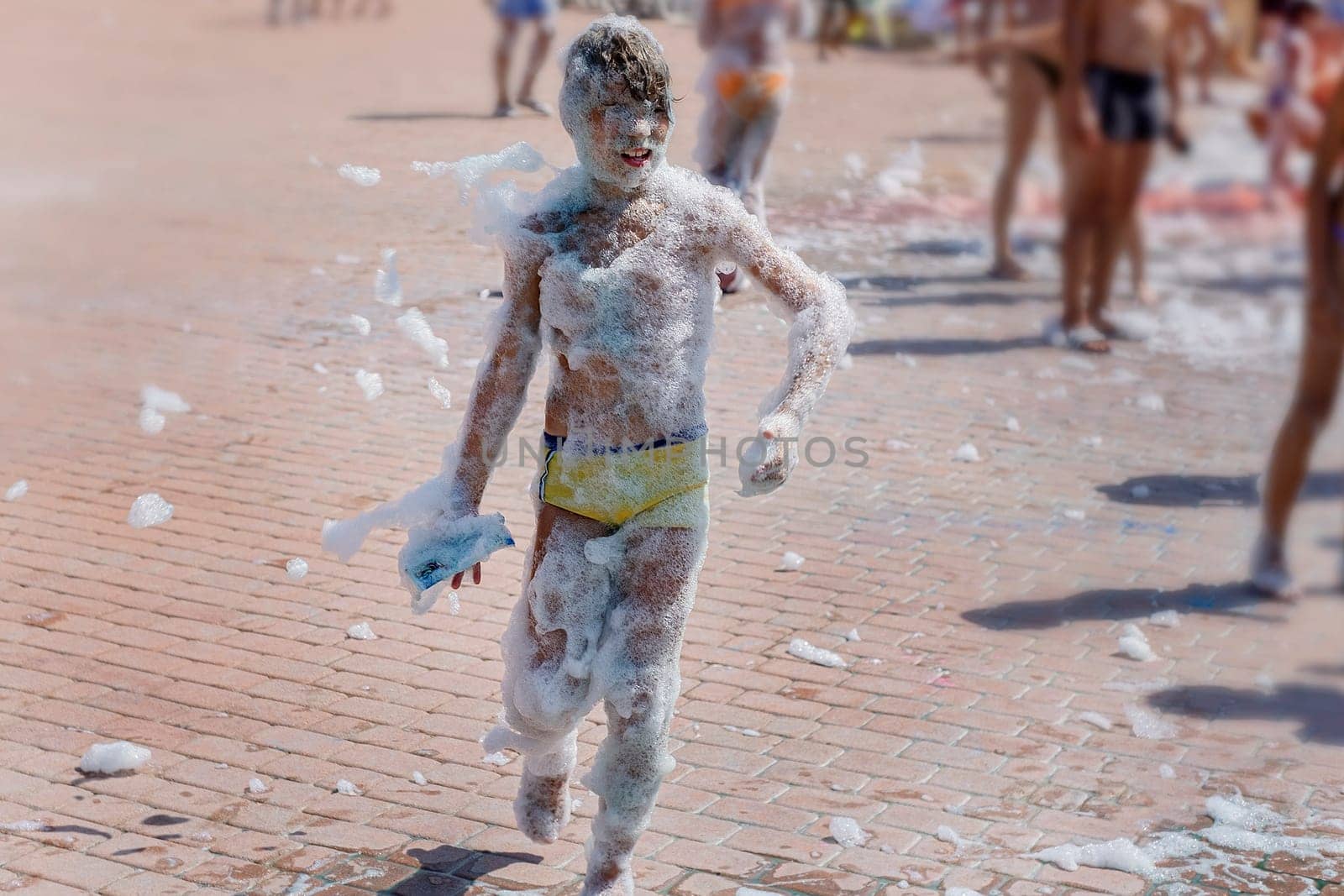 Happy boy with foam on whole body at a foam party or holiday on a sunny hot summer day.