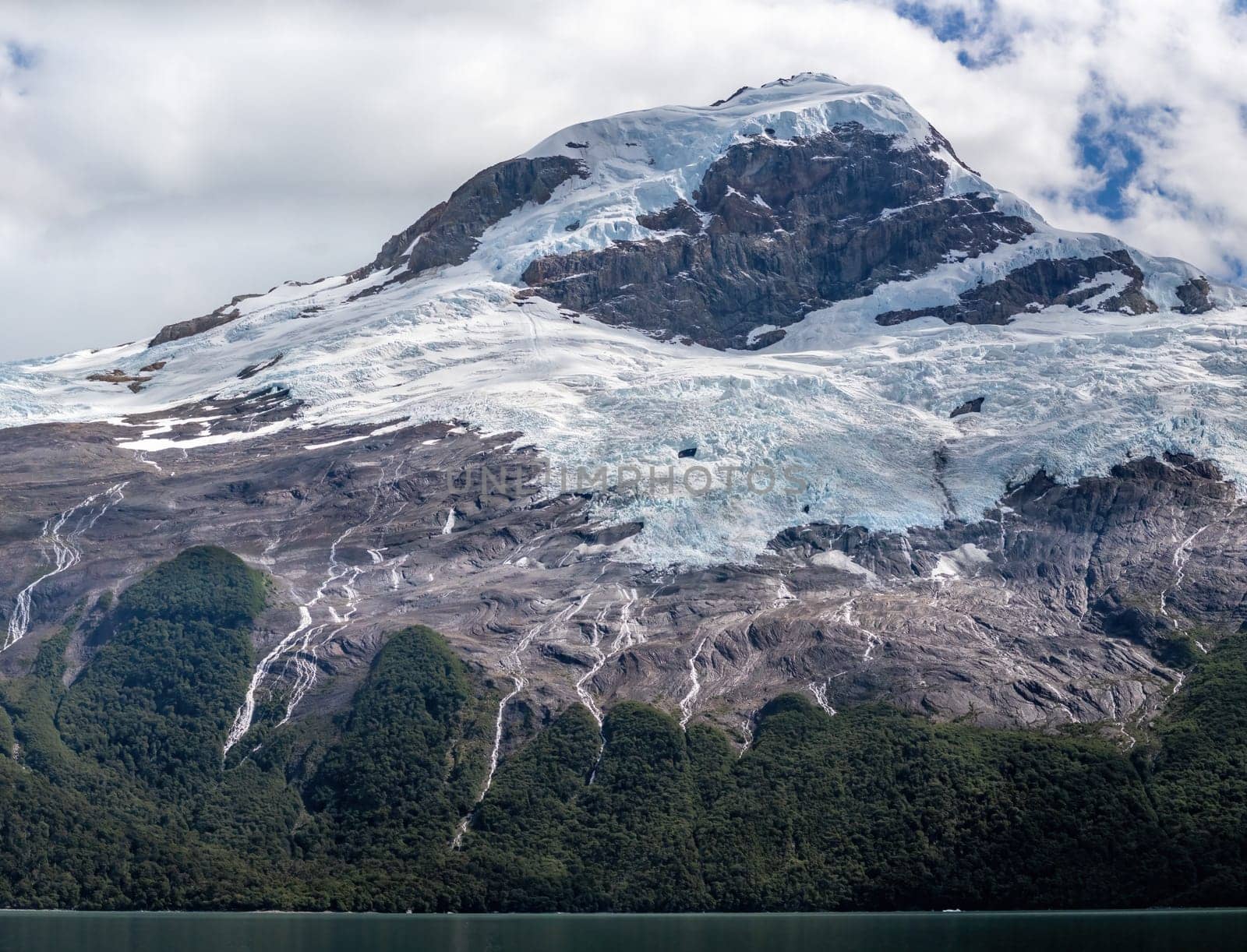 Glacier flows down a mountain into a peaceful lake.