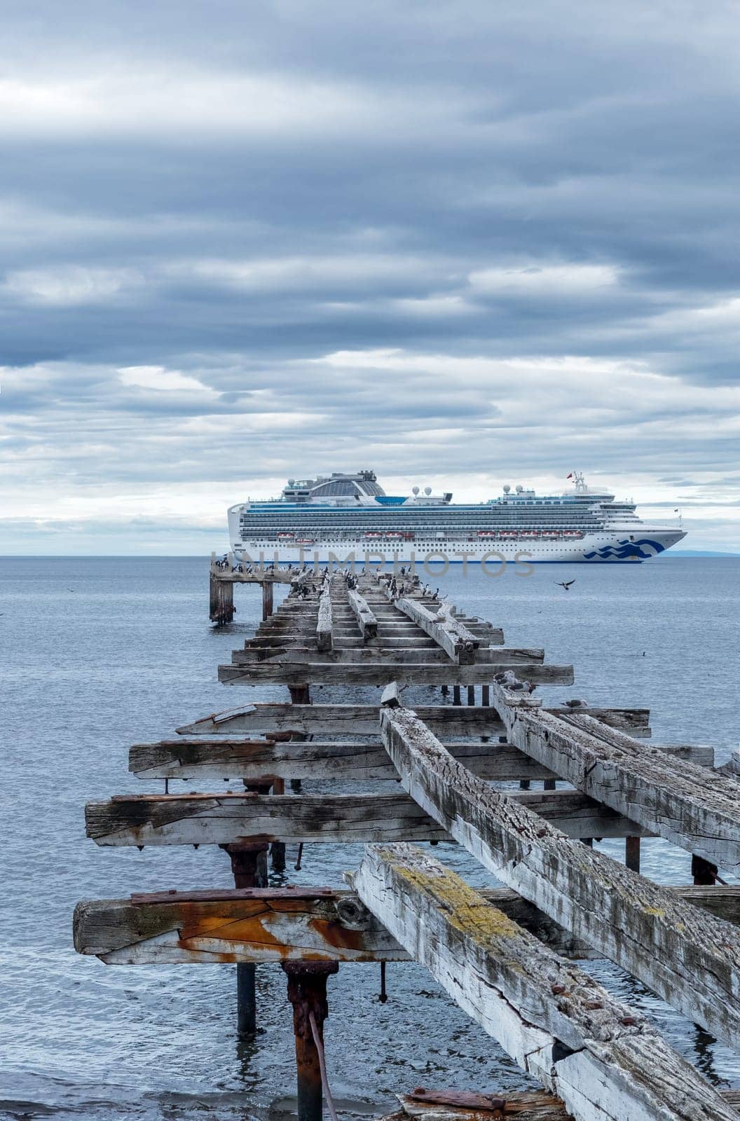 Aged pier meets modern cruise ship beneath a striking cloudy sky at sea.
