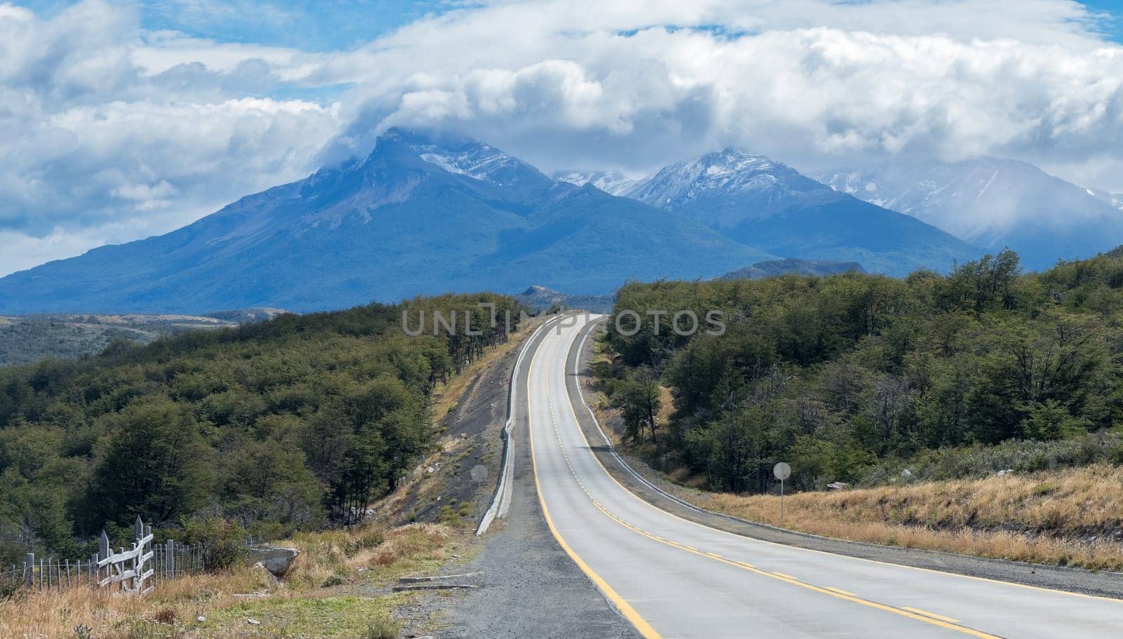 A vacant, curvy road leads to mountains under cloudy skies.
