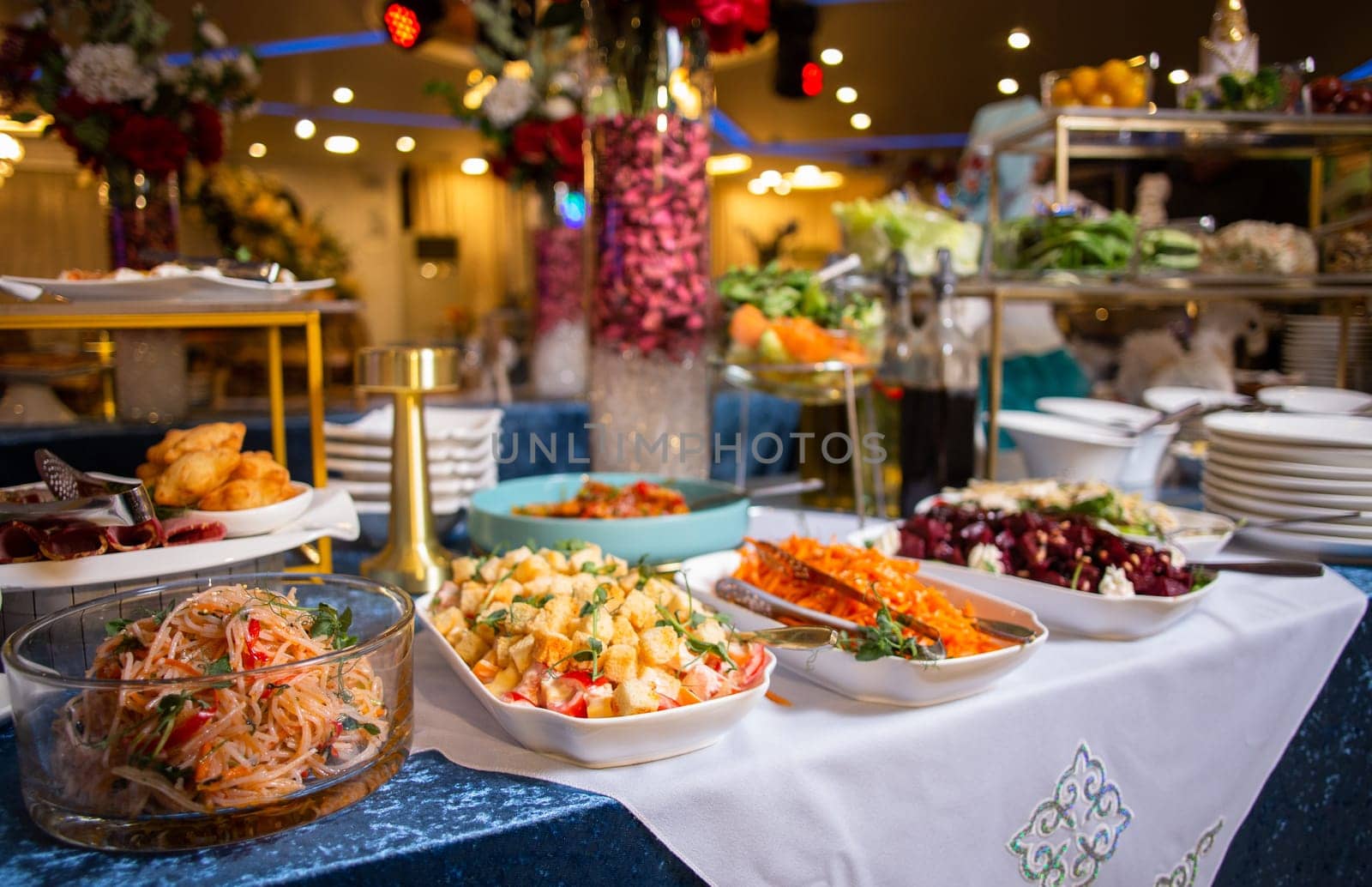 Buffet table with salads, appetizers desserts in banquet hall. Long table with white tablecloth. Variety of food choices.