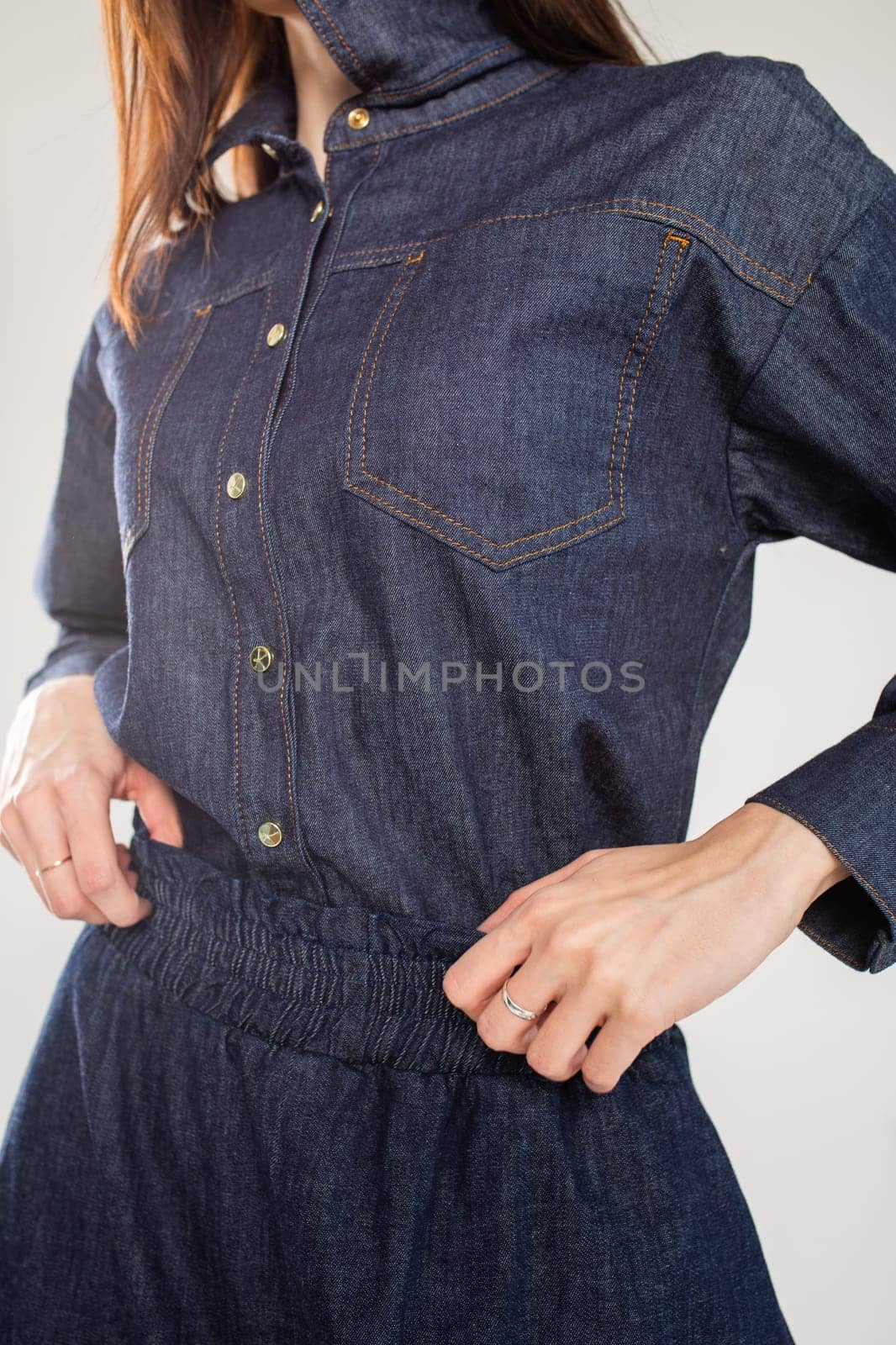 A young woman in a blue denim shirt dress with a collar and long sleeves. Fitted at the waist with a stretchy waistband.