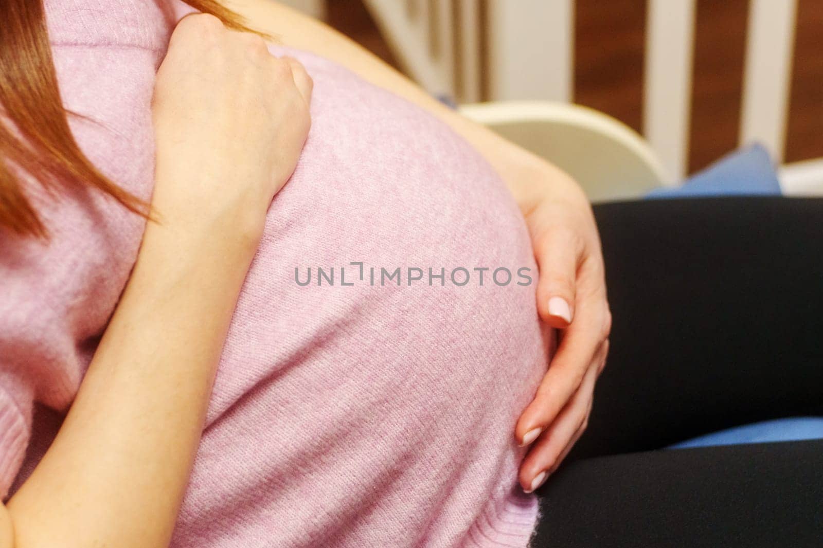 Woman is holding her stomach while sitting in a chair. A pregnant woman is expecting a baby
