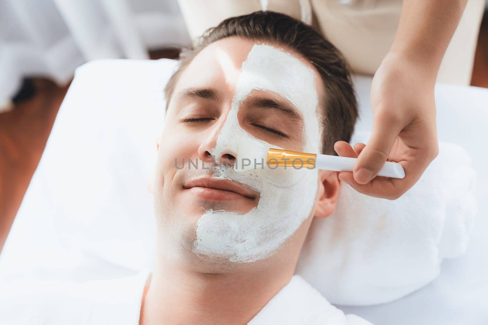 Serene ambiance of spa salon, man customer indulges in rejuvenating with luxurious face cream massage with modern daylight. Facial skin treatment and beauty care concept. Quiescent