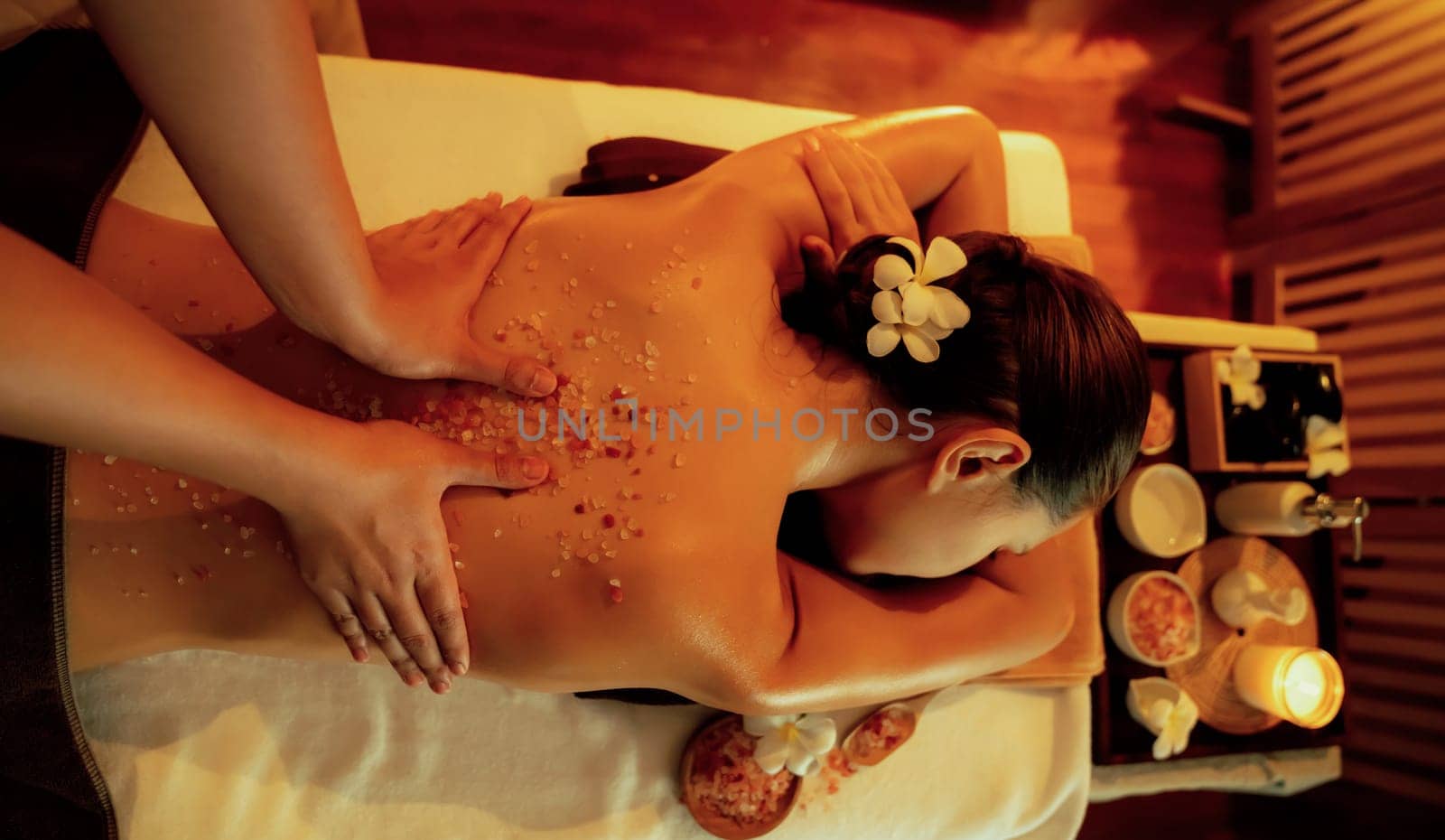 Woman customer having exfoliation treatment in luxury spa salon with warmth candle light ambient. Salt scrub beauty treatment in Health spa body scrub. Quiescent