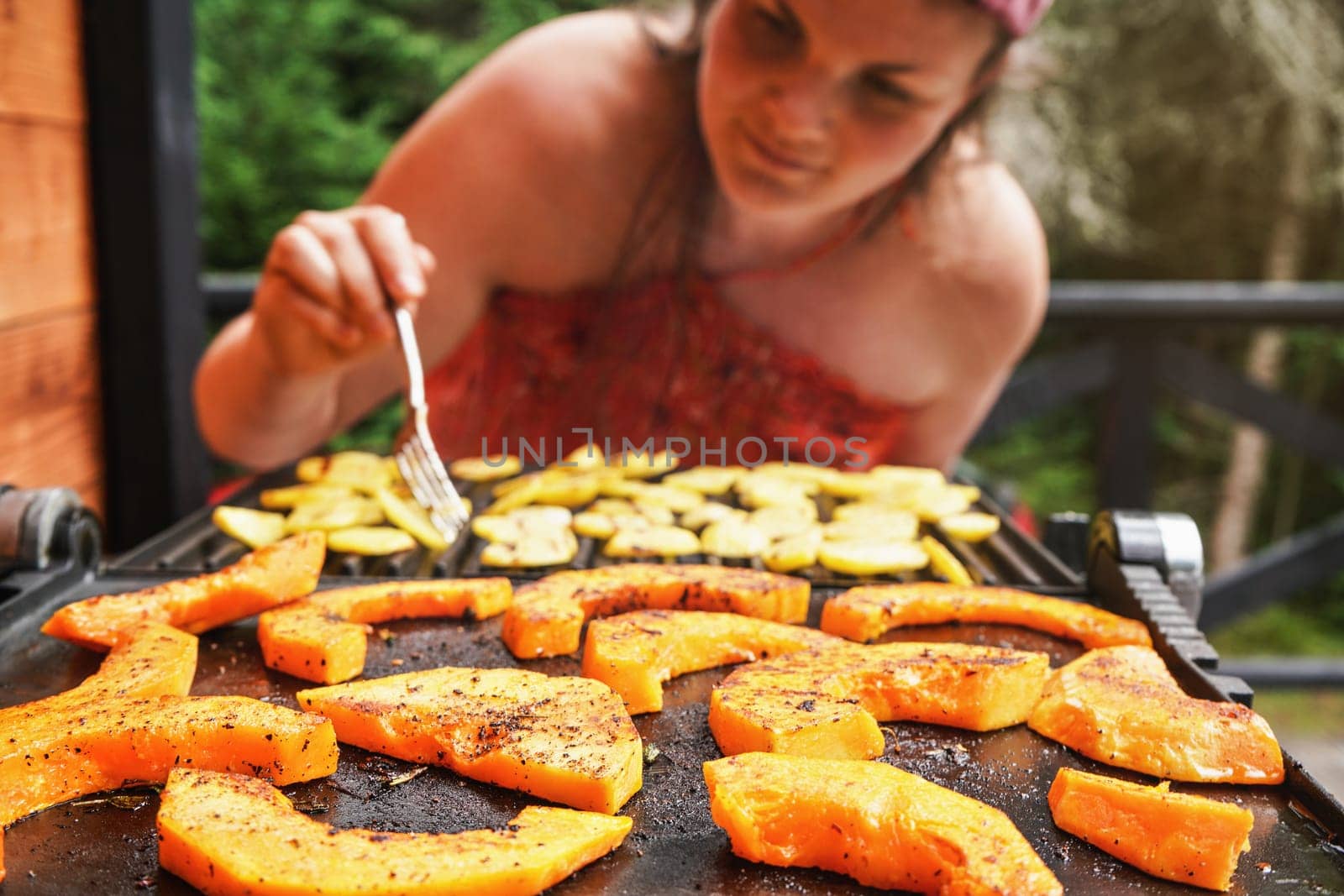 Butternut squash pieces grilled on electric grill, focus on bright orange vegetables seasoned with spice, blurred young woman in background by Ivanko