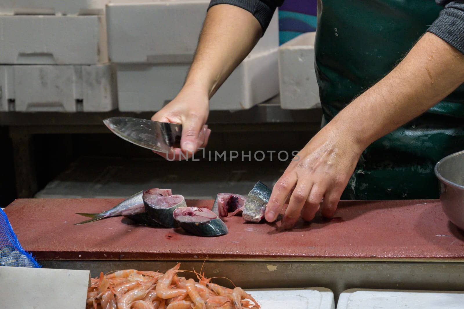 Closeup of male worker's hands cutting fish with knife at table.