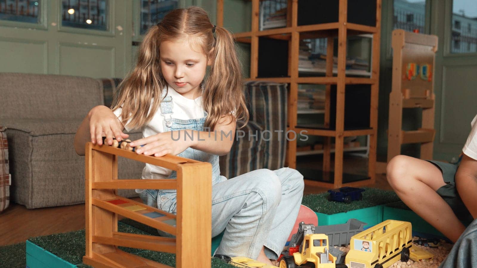 Caucasian girl sits at sand box while placed car model at slope toy. Erudition. by biancoblue