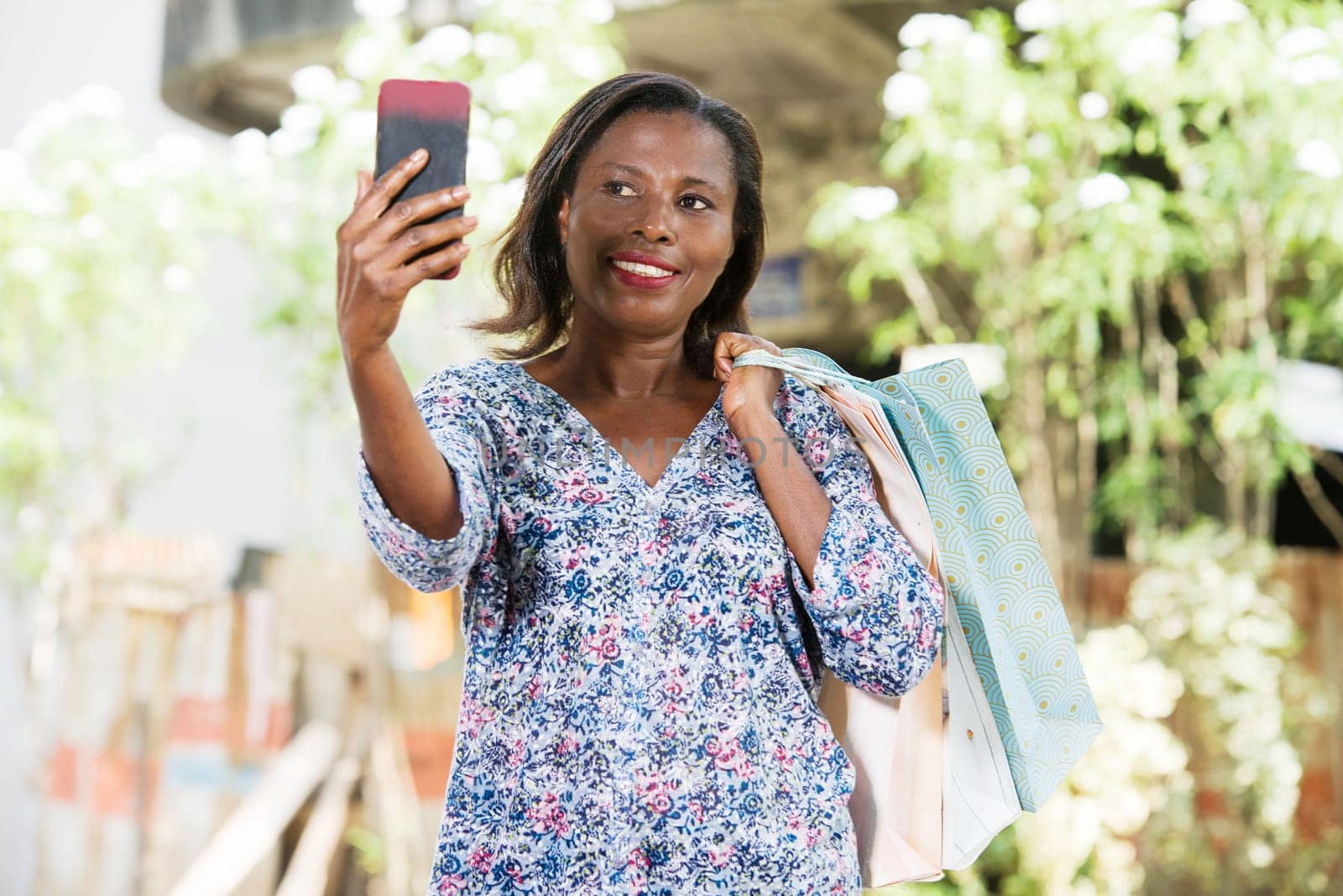 young woman standing outdoors after shopping looking at mobile phone while smiling.
