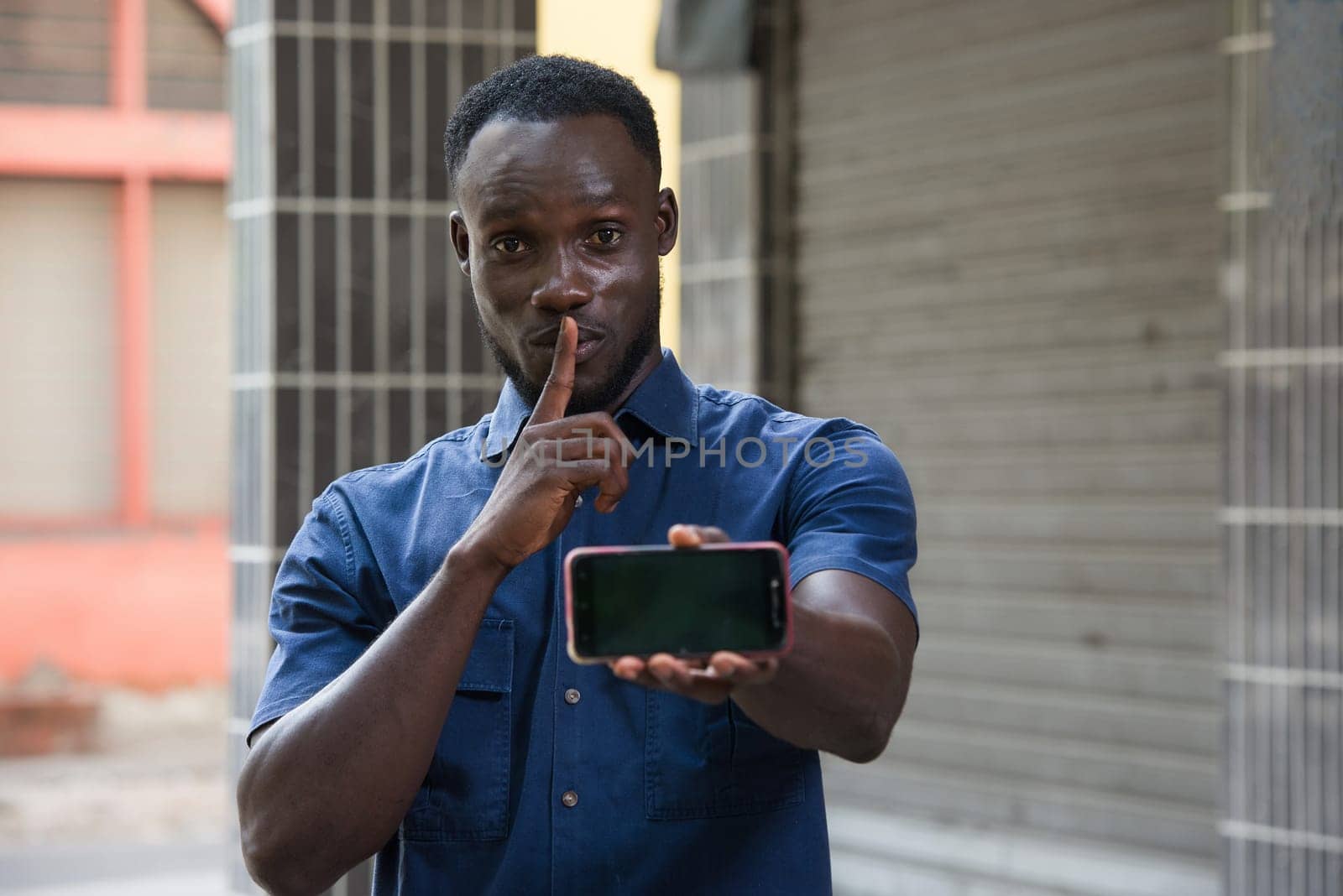 excited man expressing surprise on face and showing phone screen and having silence gesture with finger on mouth