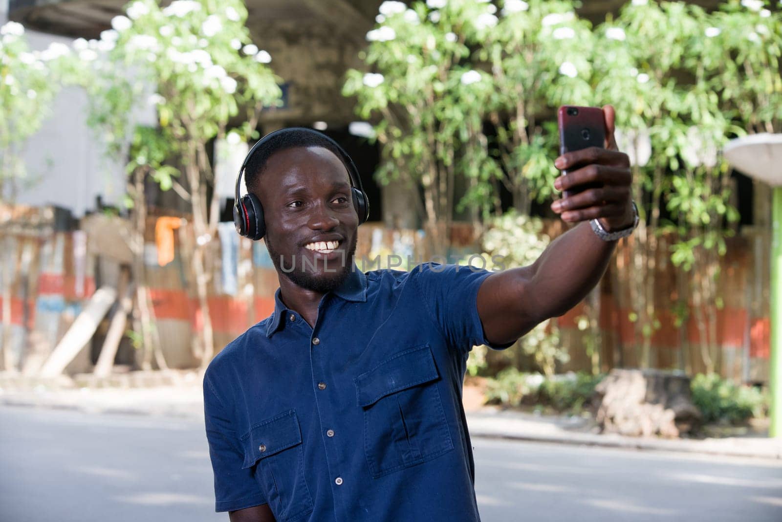 Man listens to music with headphones using a cell phone and makes photos with his phone outside.