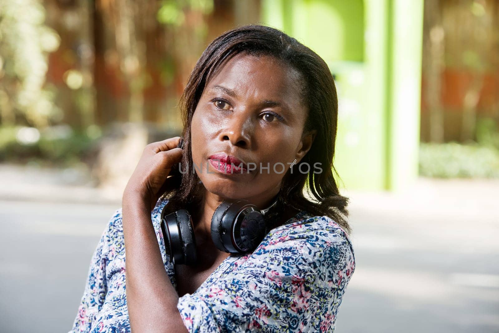 young woman standing outdoors stroking her hair with headphones on her neck.