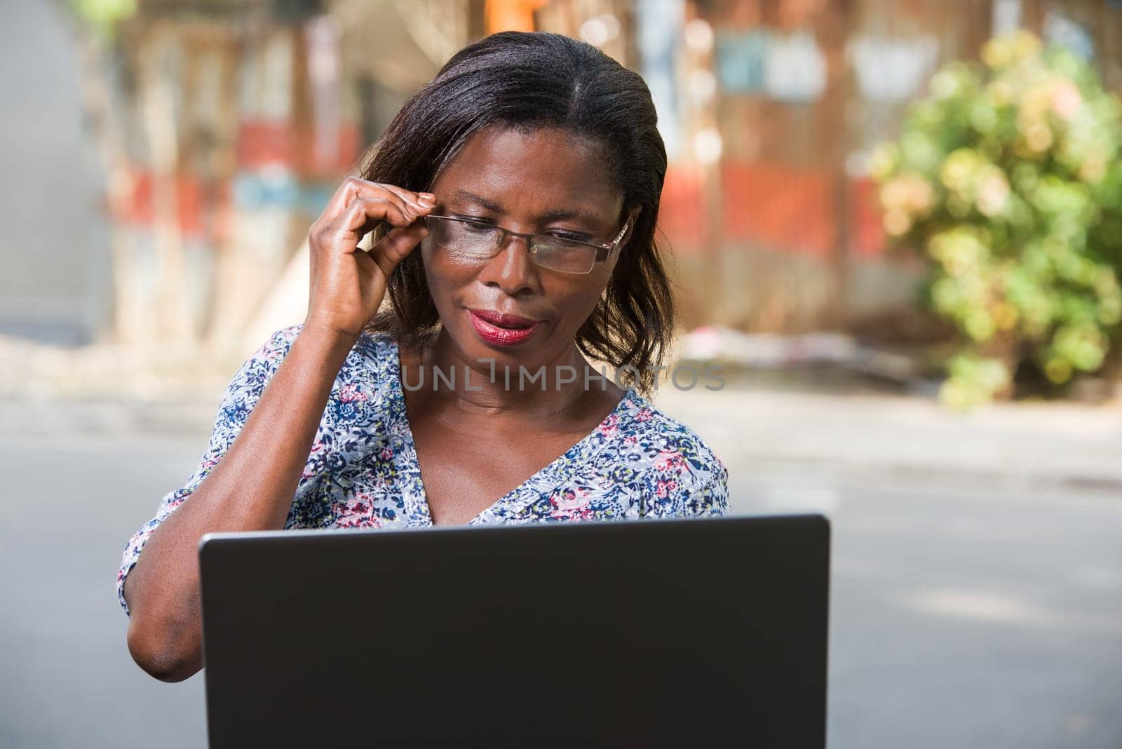 young woman sitting outside in glass looking at laptop smiling.