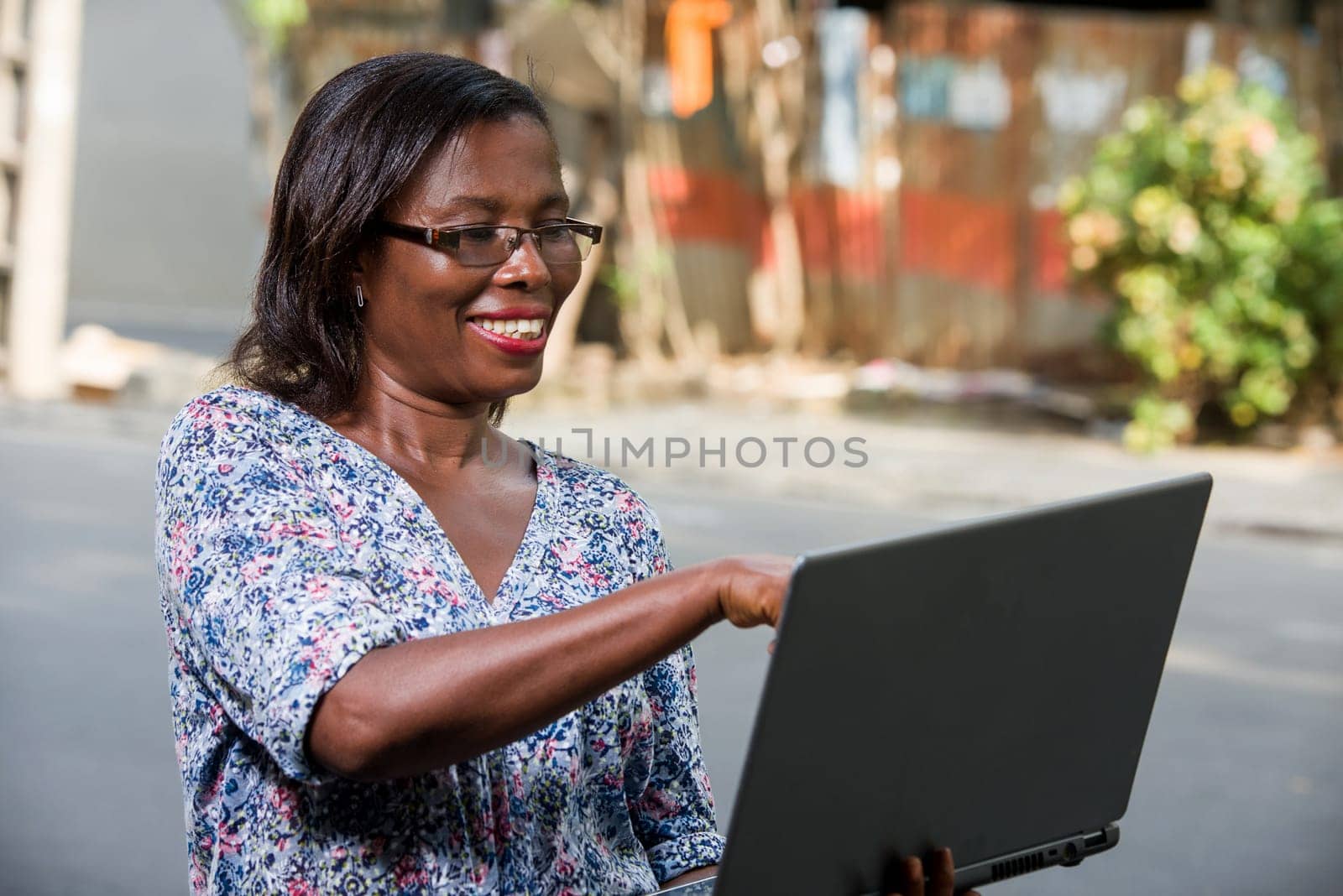 young woman sitting outside in glasses looking at laptop laughing.