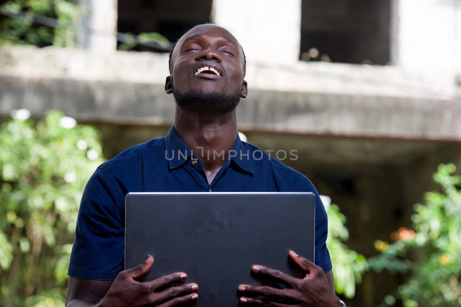 young man sitting outdoors smiling with his eyes closed with laptop.