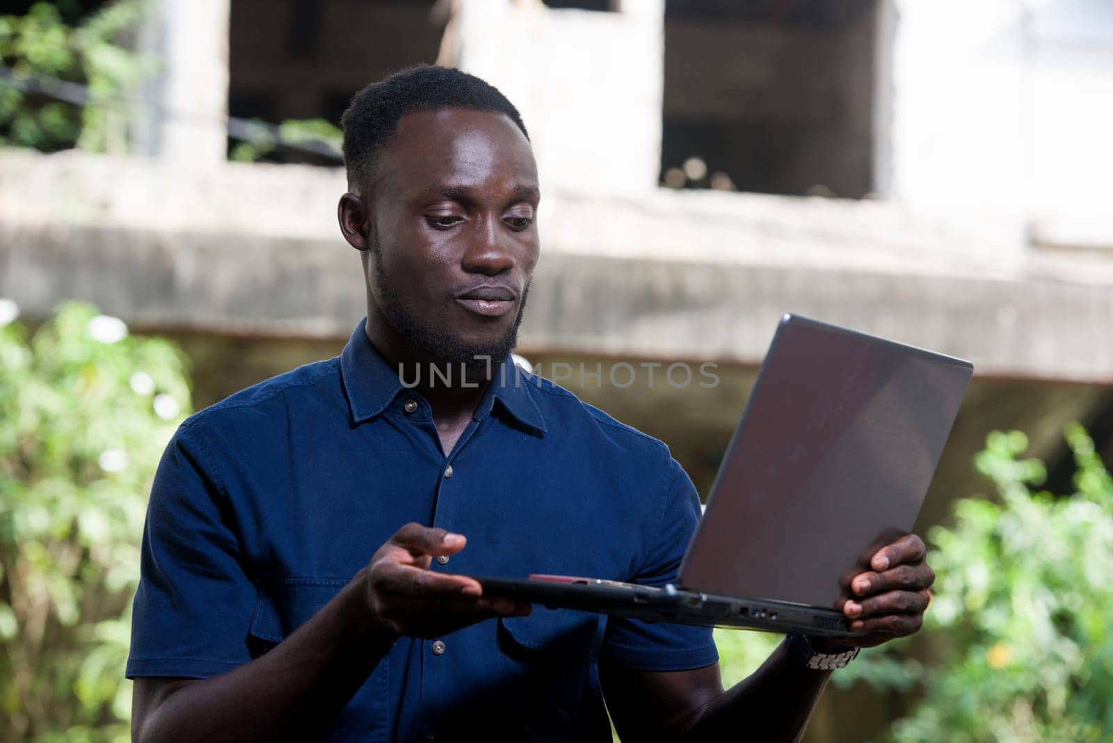young man sitting outdoors presenting laptop .