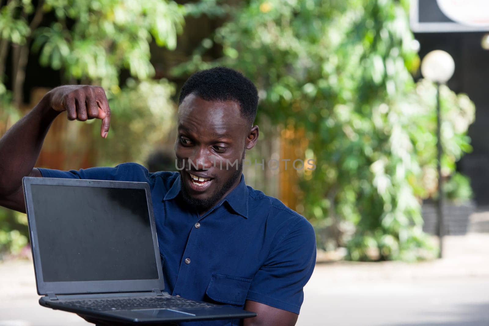 young man sitting outdoors showing laptop smiling.