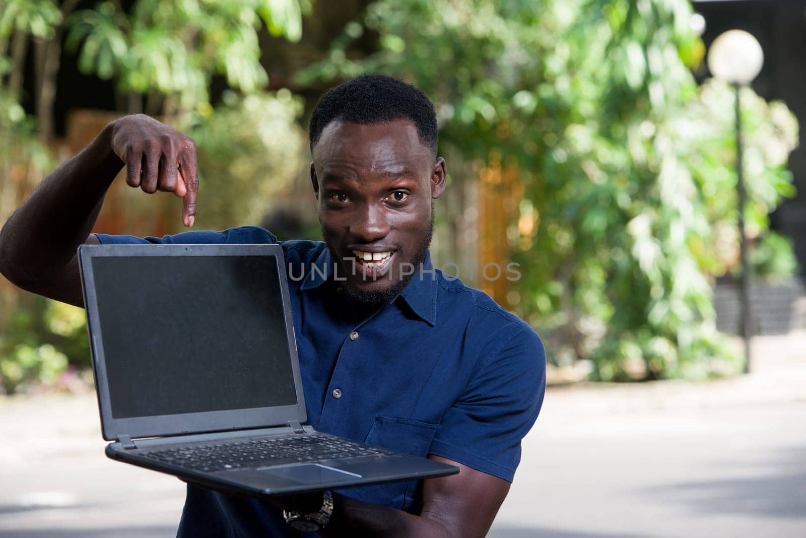 young man sitting outdoors showing laptop smiling.