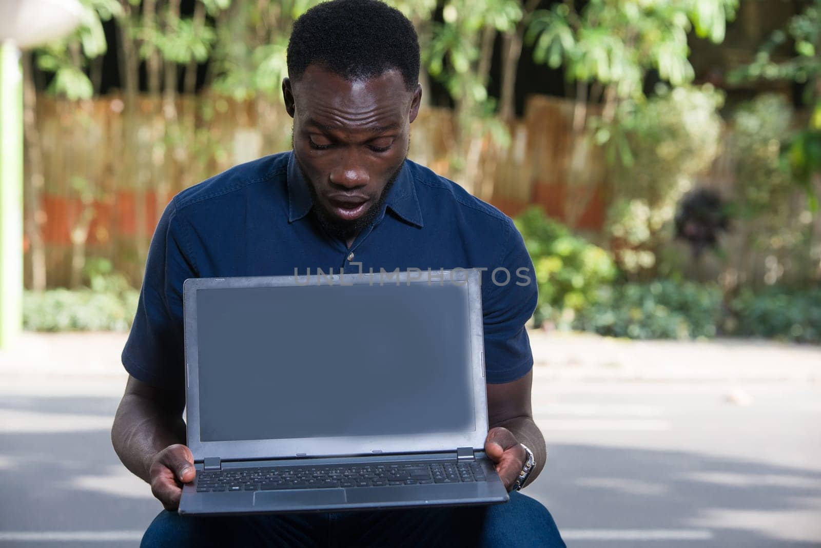 young man sitting outdoors looking at laptop with surprise.