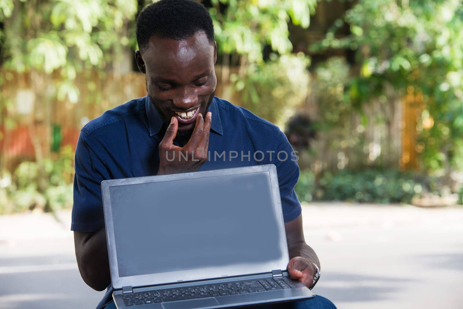 young man sitting outdoors looking at laptop while smiling.