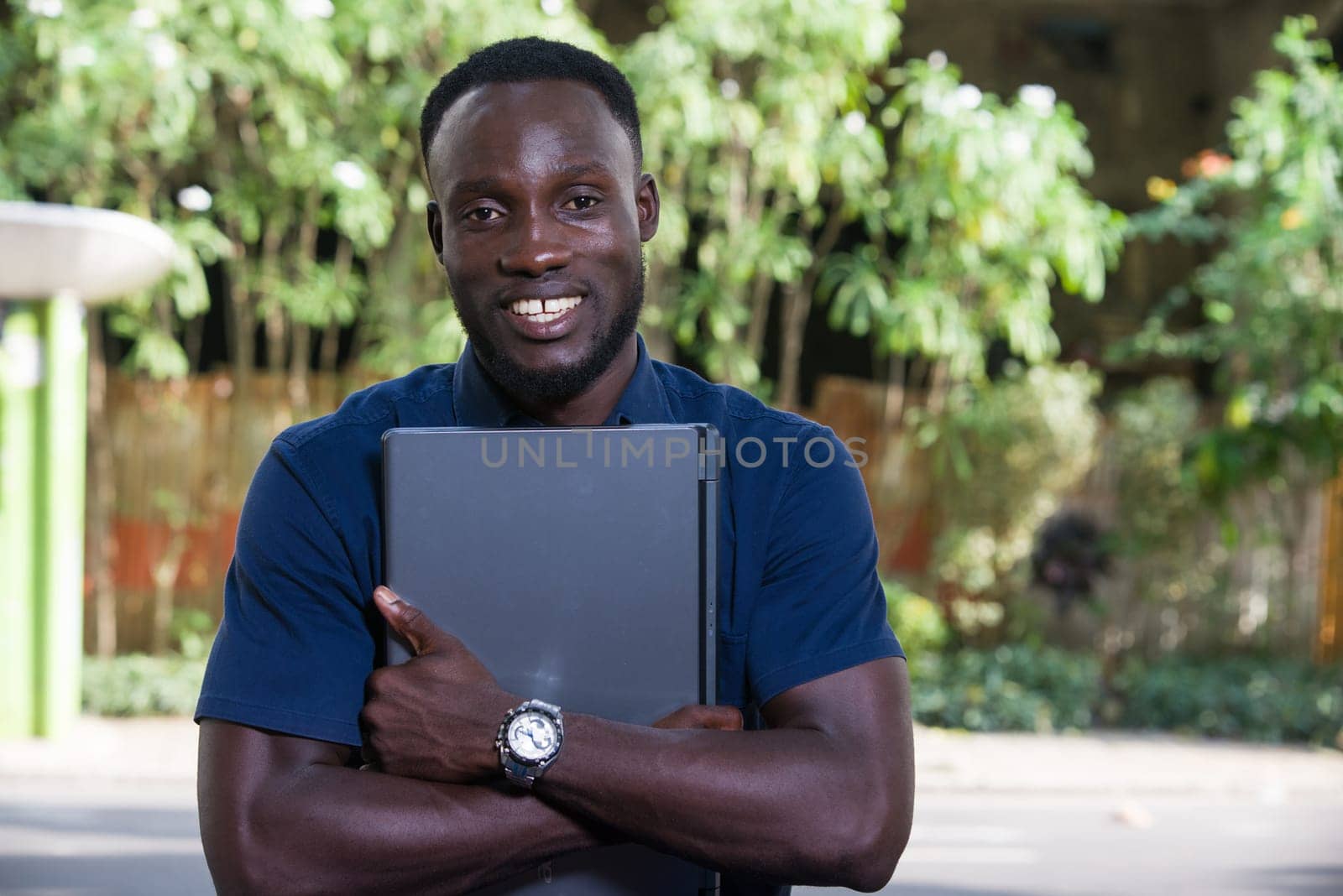 young man sitting outdoors with laptop computer looking at camera smiling.