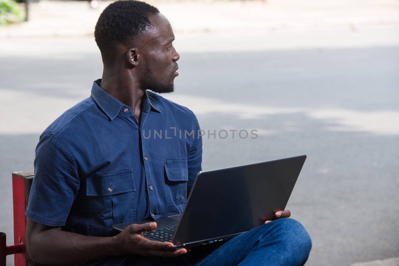 young man sitting outdoors with laptop watching something surprised.