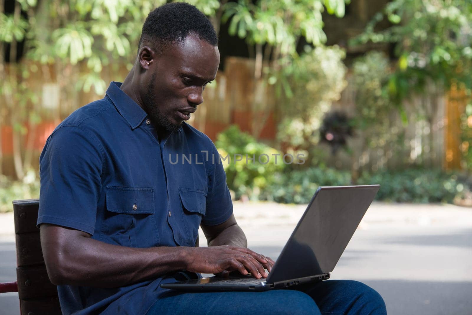 young man sitting outdoors looking at laptop with discontent.