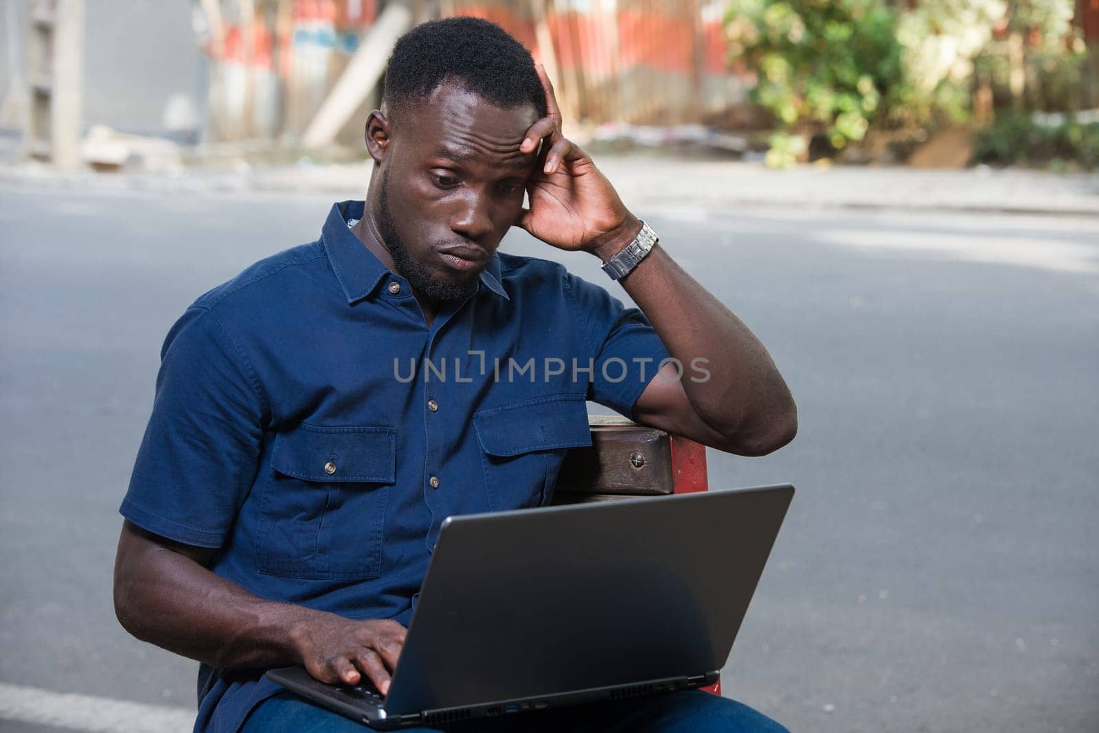 young man sitting outdoors with laptop thinking.