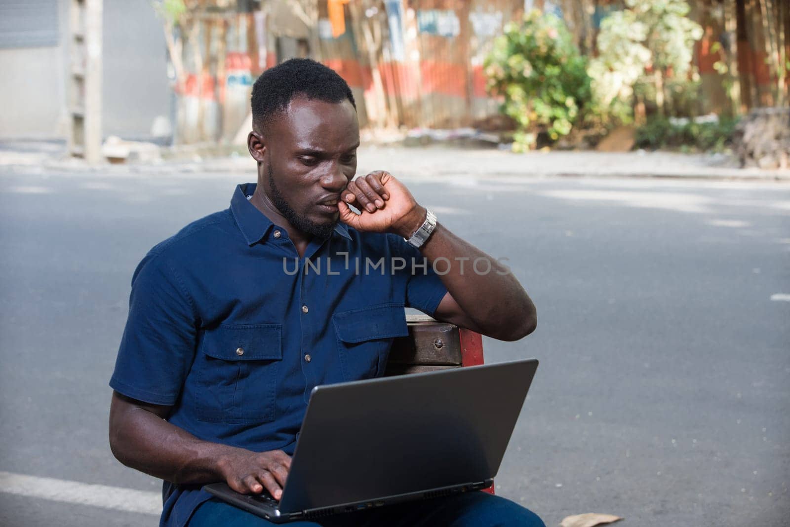 young man sitting outdoors with laptop thinking.