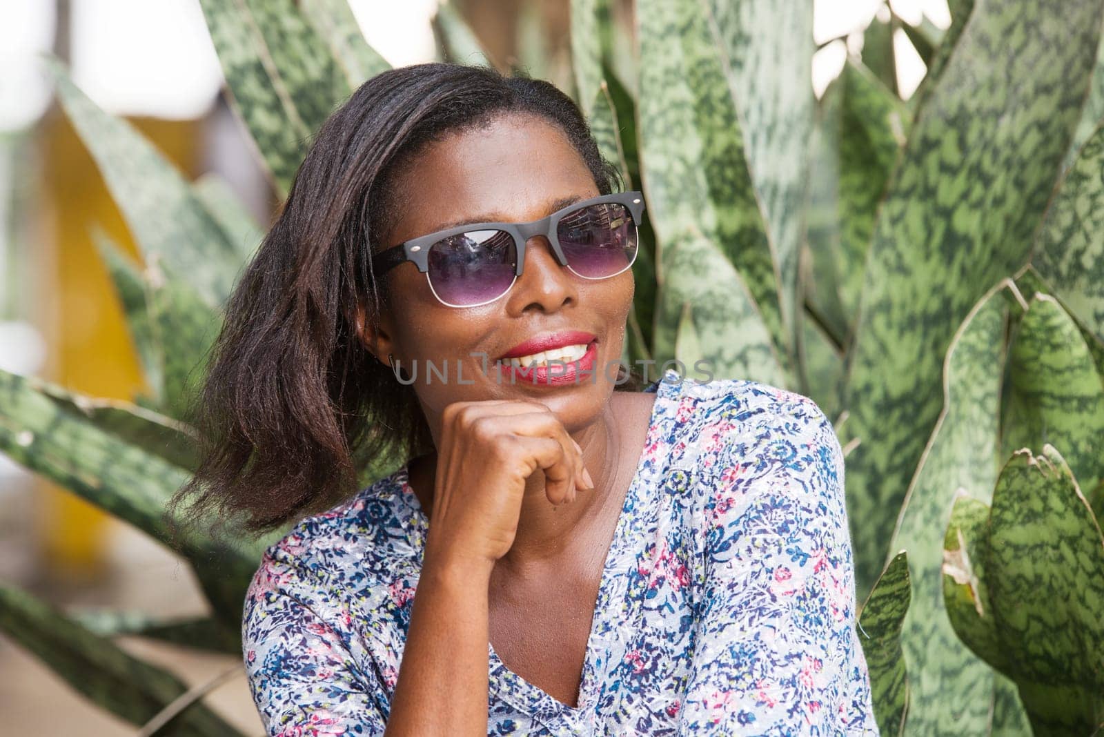 young woman sitting in a park looking at the camera hand under the chin smiling.