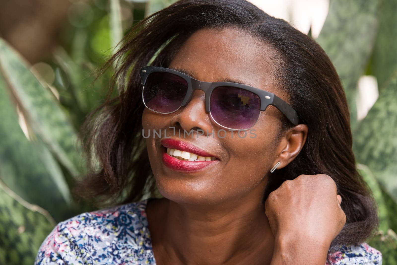 young woman sitting in a park in sunglasses watching the camera smiling.