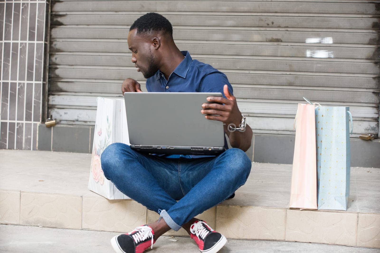 young man sitting on the floor with laptop watching in shopping bag.