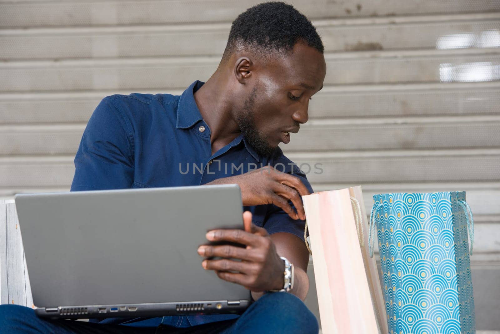 young man sitting on the floor with laptop watching in shopping bag.