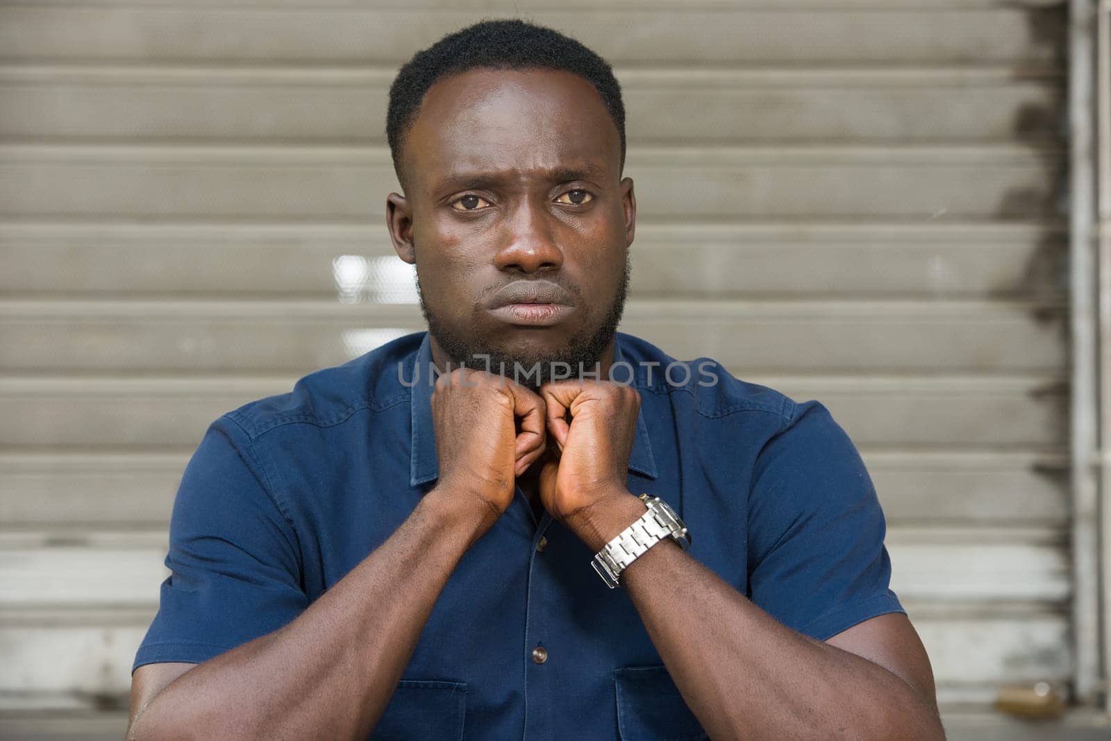 young man in blue shirt sitting outdoors thinking of fists under chin.