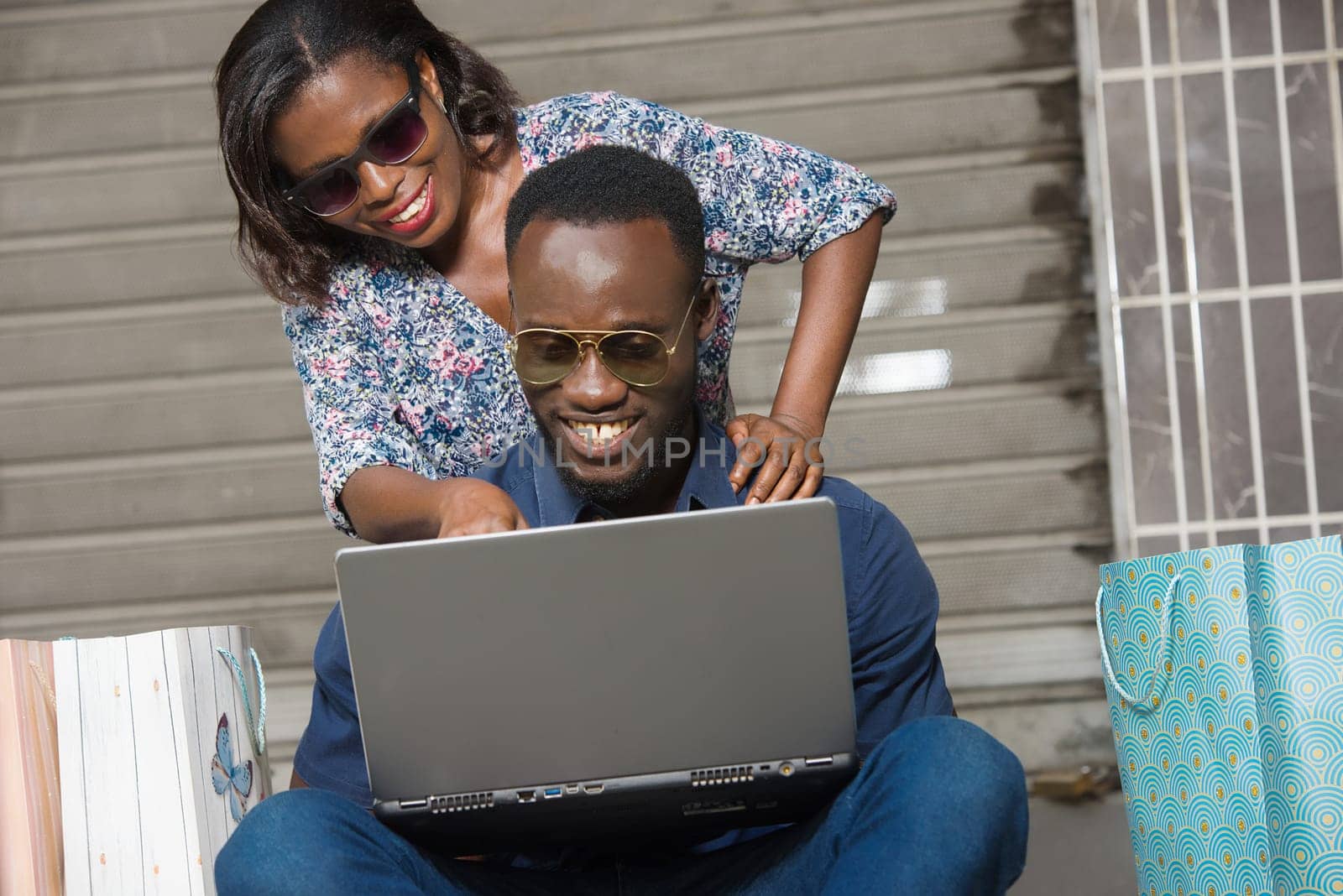 Happy couple using a laptop sitting outside and spending time together after doing a shopping