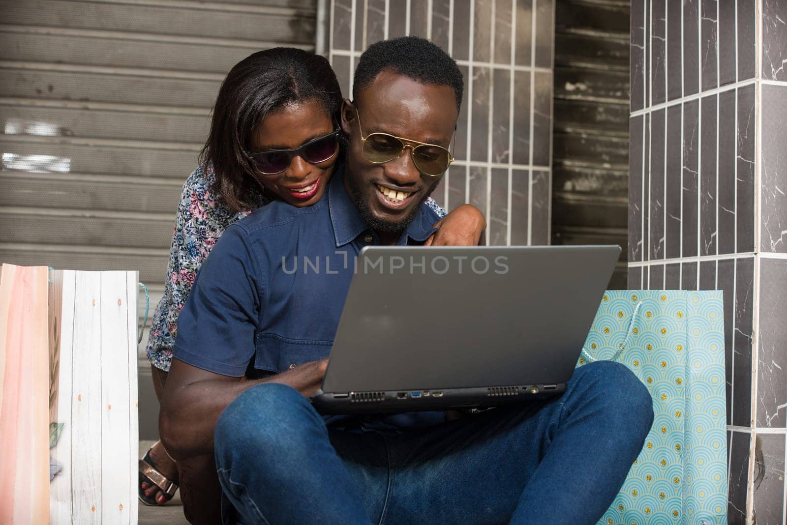 Happy couple using a laptop sitting outside and spending time together after doing a shopping