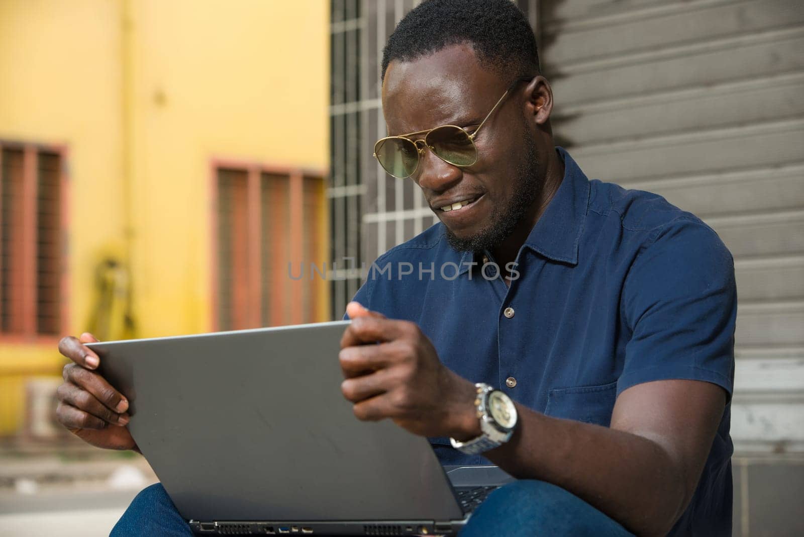 young man sitting outside thinking about looking at laptop.