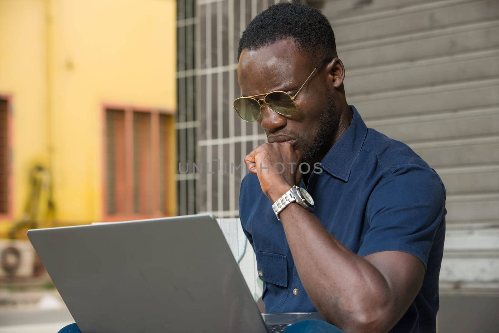 young man sitting outside thinking about looking at laptop.