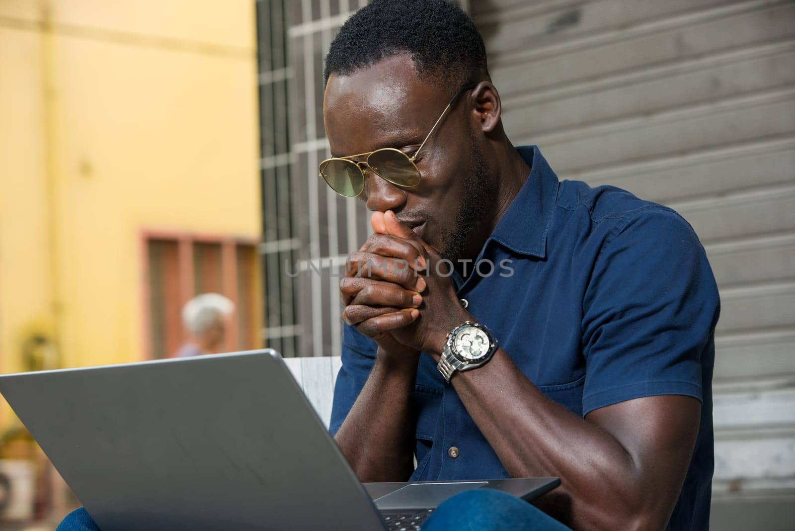 young man sitting outside looking at laptop smiling.