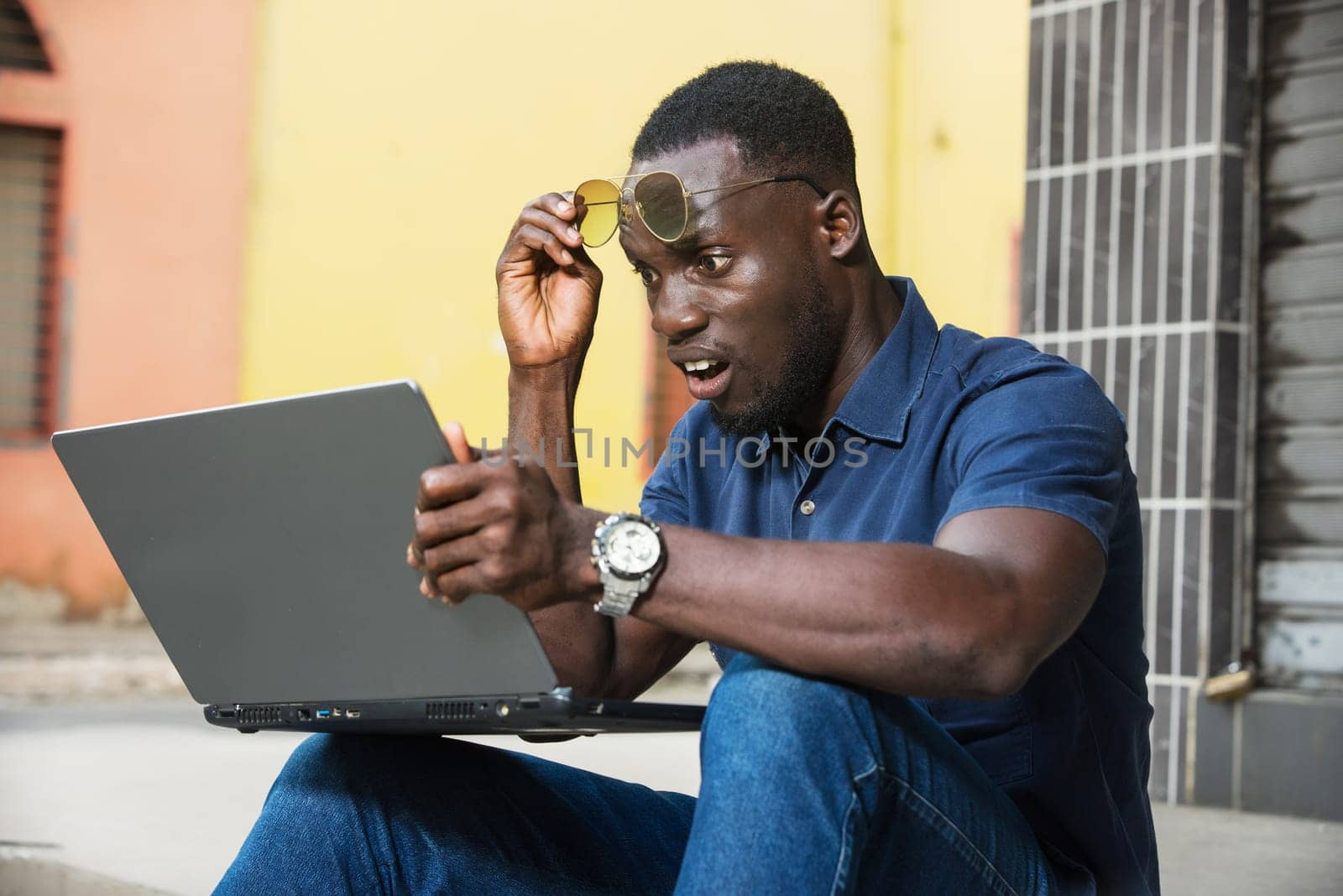 young man sitting outside looking at laptop with anger.