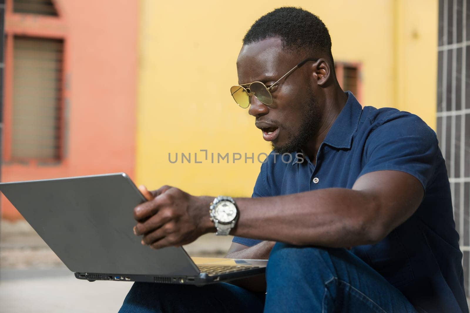 young man sitting outside looking at laptop with surprise