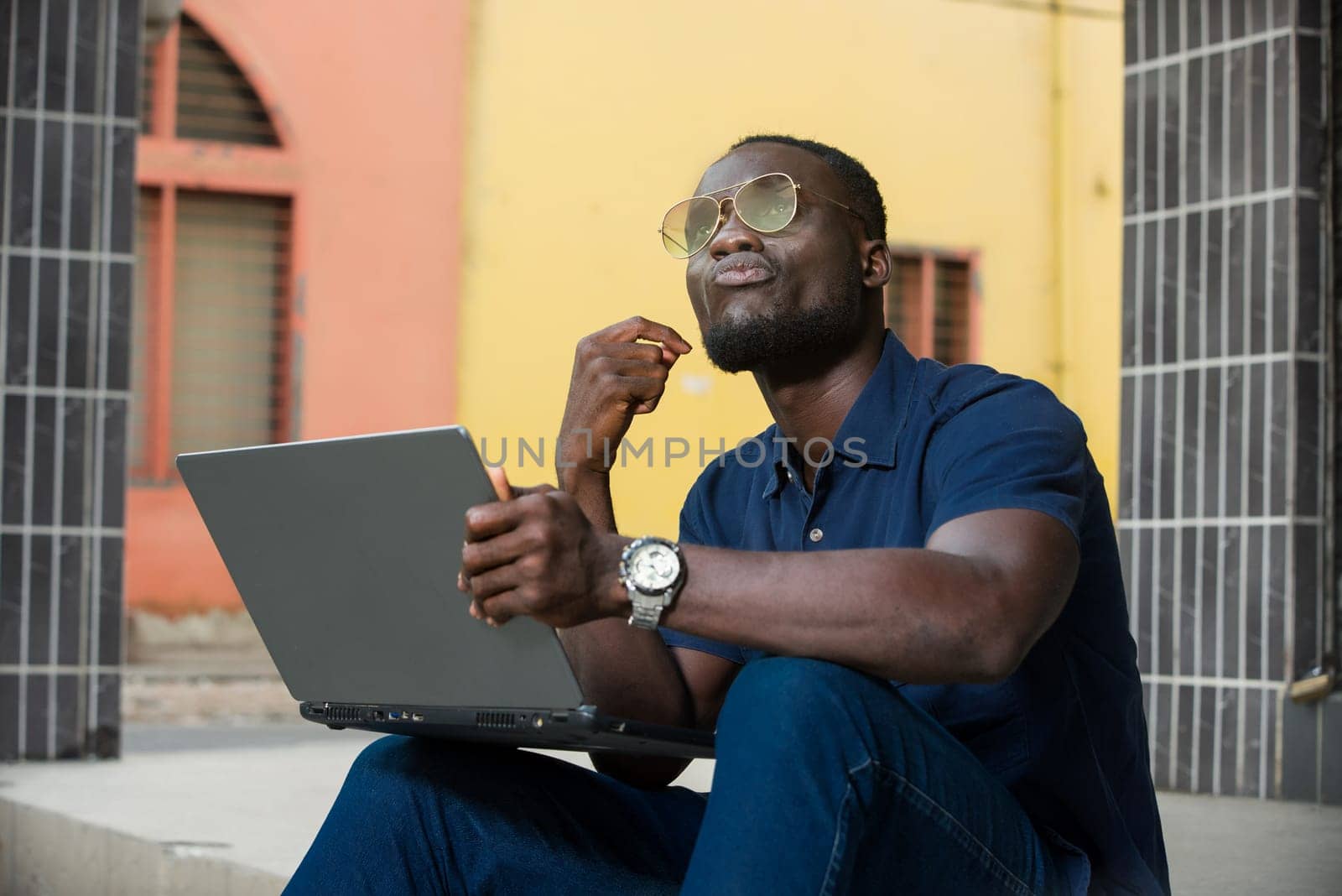 young man sitting outside looking up with laptop in hand.
